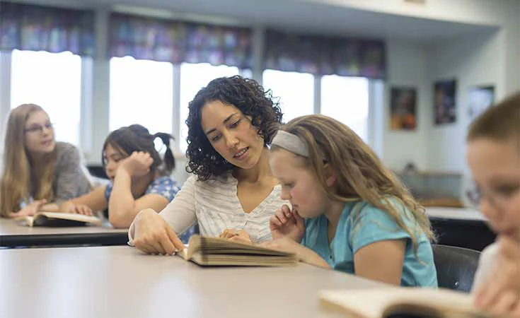 female teacher helping a young student with a reading assignment