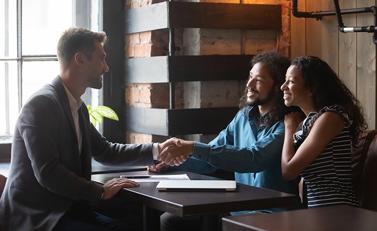 white male professional shaking hands with smiling black couple